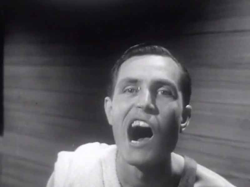 Still from The Fanfare music video for artist Tom Hickox — archive footage from a 1940s PSA where a man checks his teeth in a mirror